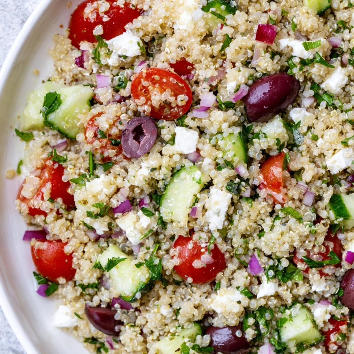 A close-up of Mediterranean Quinoa Salad with Cherry Tomatoes, featuring bright red tomato halves, green cucumber cubes, and Kalamata olives, perfect for a refreshing summer lunch.