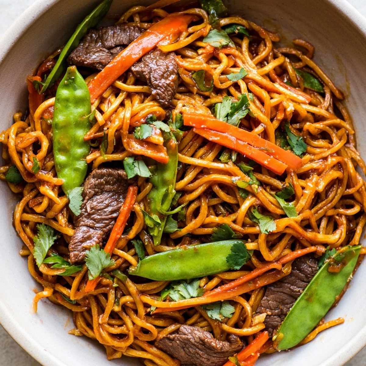 A close-up of Spicy Beef Noodles with Vegetables garnished with cilantro and sesame seeds on a rustic plate.