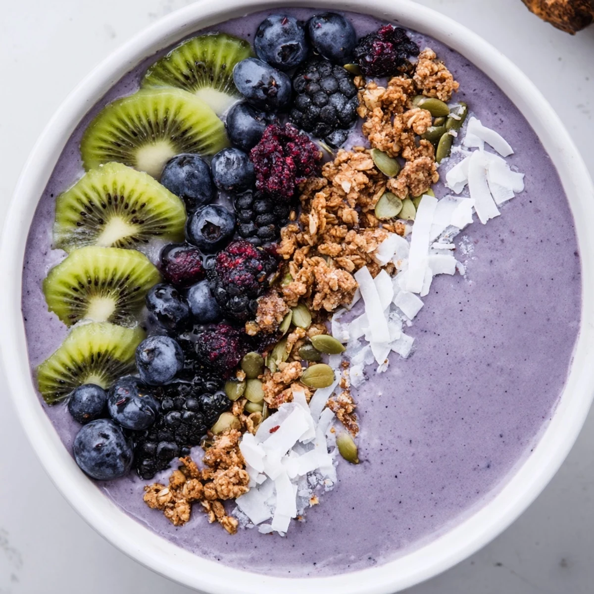 Creamy frozen winter berry smoothie base swirled in a bowl, topped with crunchy granola, fresh kiwi, and pumpkin seeds.  