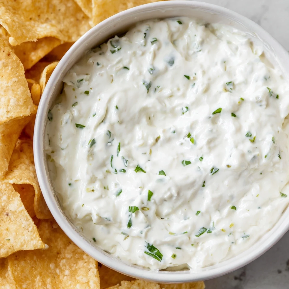 Fresh, creamy Creamy Dip Bowl with Chips garnished with chopped chives and parsley, paired with golden potato and tortilla chips for a crunchy snack.