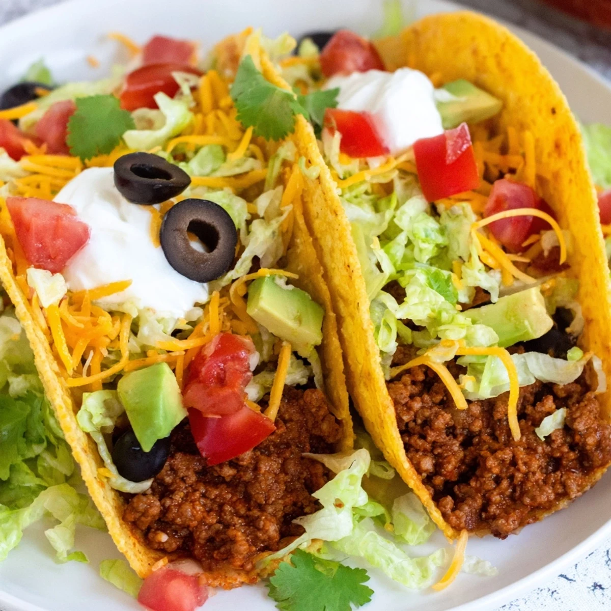 Crispy hard taco shells filled with seasoned ground beef, topped with shredded lettuce, cheese, and fresh avocado slices.