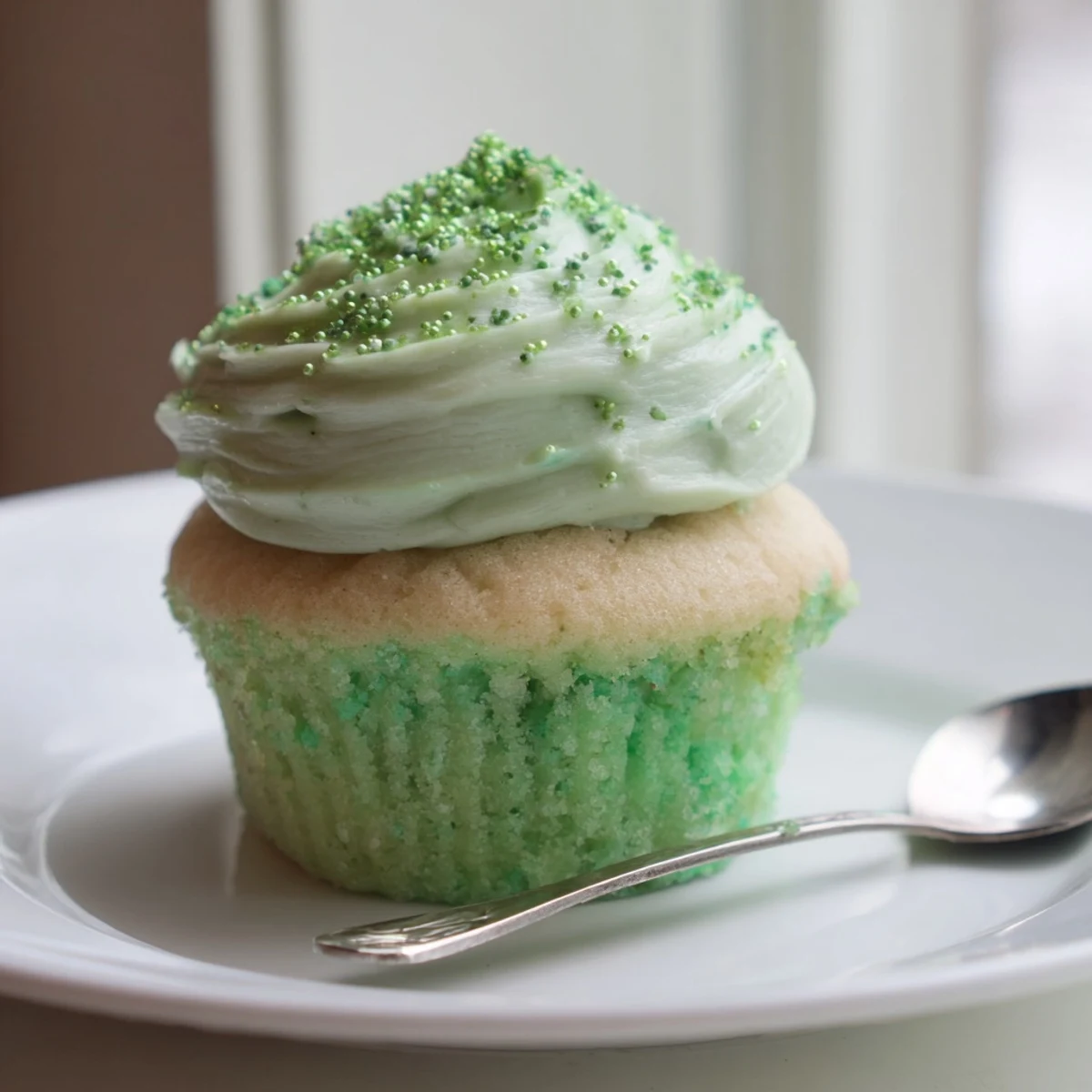 A hand gently places a shamrock-shaped sprinkle on a frosted Shamrock Shake Cupcake, highlighting the dessert's St. Patrick's Day theme.