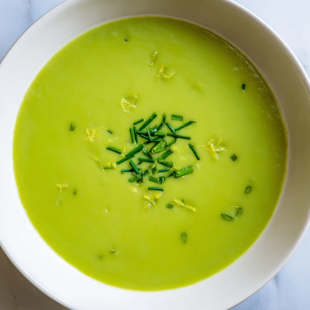 Creamy Asparagus Soup with Lemon in a rustic white bowl, garnished with fresh lemon zest and bright green chives.