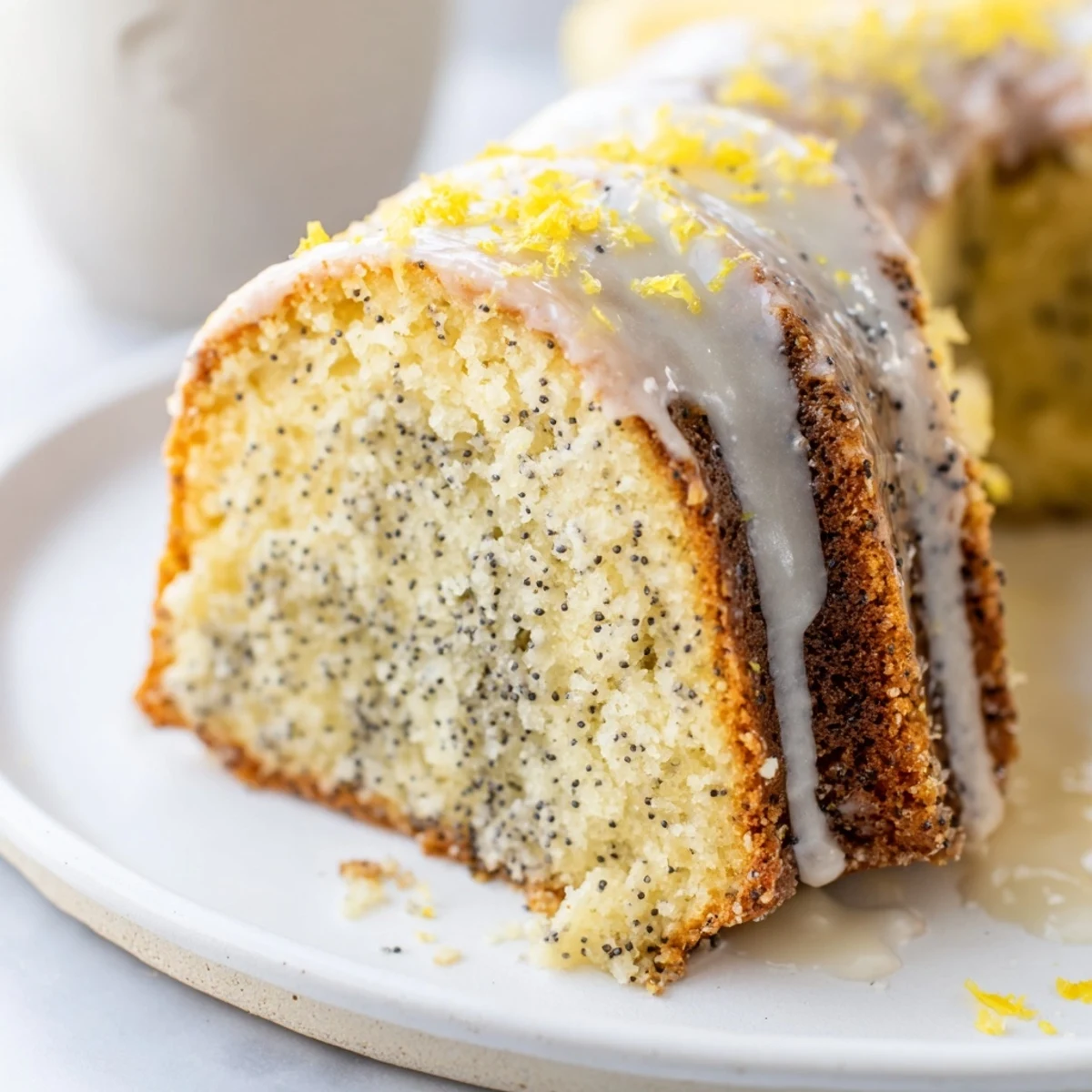 A freshly baked Lemon Poppy Seed Bundt cake shows a tender crumb, drizzled with tangy lemon glaze and sprinkled with extra poppy seeds.