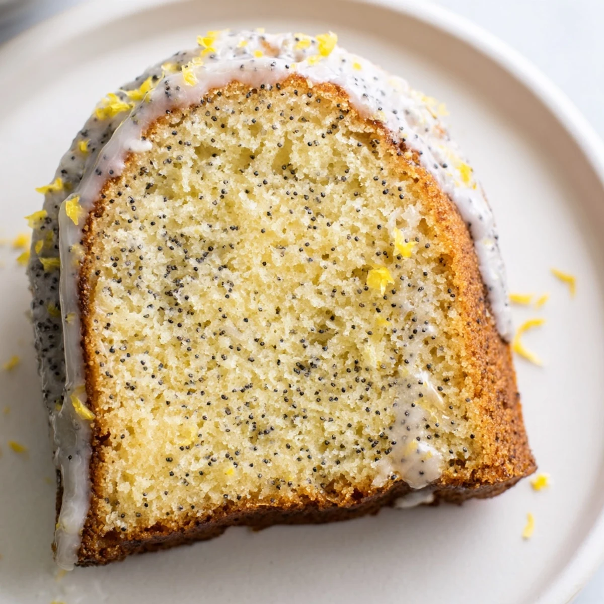 Moist Lemon Poppy Seed Bundt cake on a cake stand, with a slice cut to reveal the bright, seedy interior and zesty glaze.