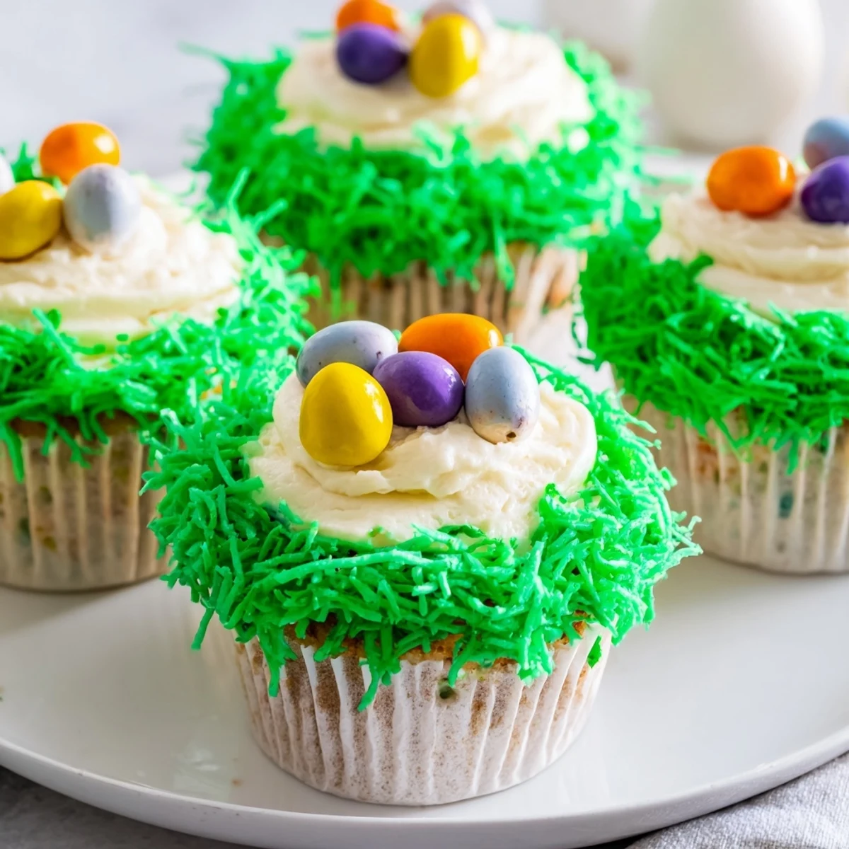 Frosted Easter Basket Cupcakes topped with green coconut grass and mini candy eggs arranged in a nest.