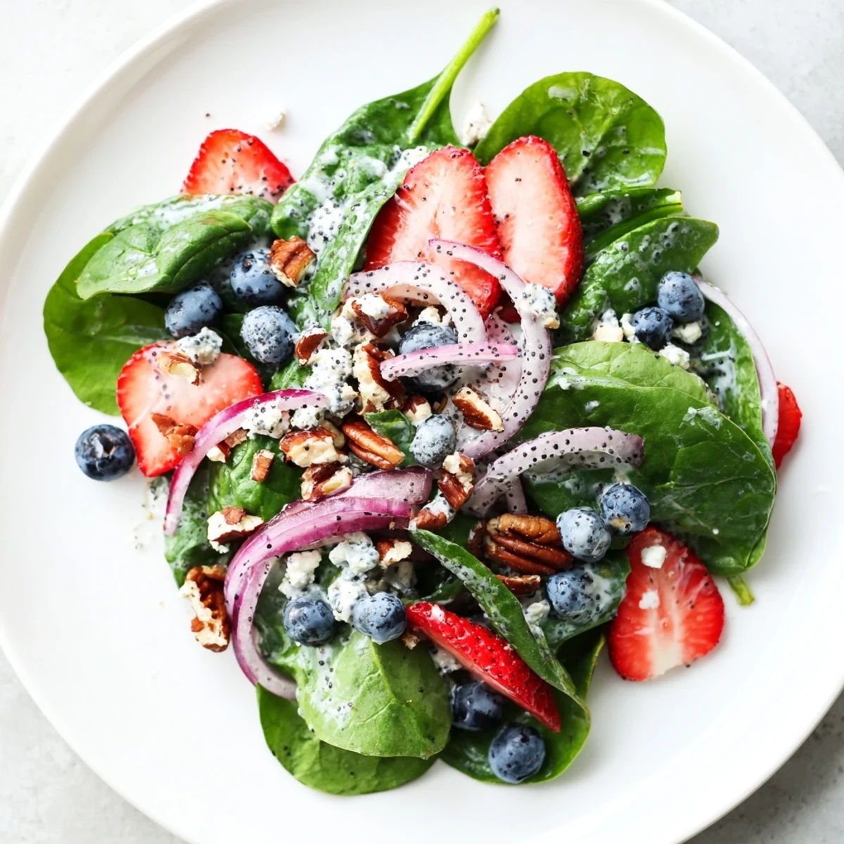 Light lunch Strawberry Spinach Salad with Poppy Seed Dressing, plated beside a glass of crisp Sauvignon Blanc, highlighting blueberries and a sprinkle of poppy seeds.