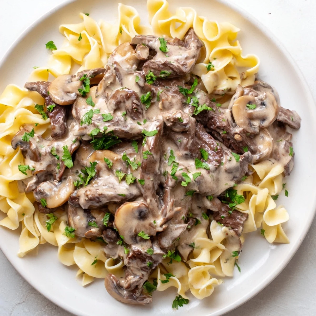 Hearty Beef Stroganoff over Egg Noodles steams in a skillet, paired with a fresh green salad.