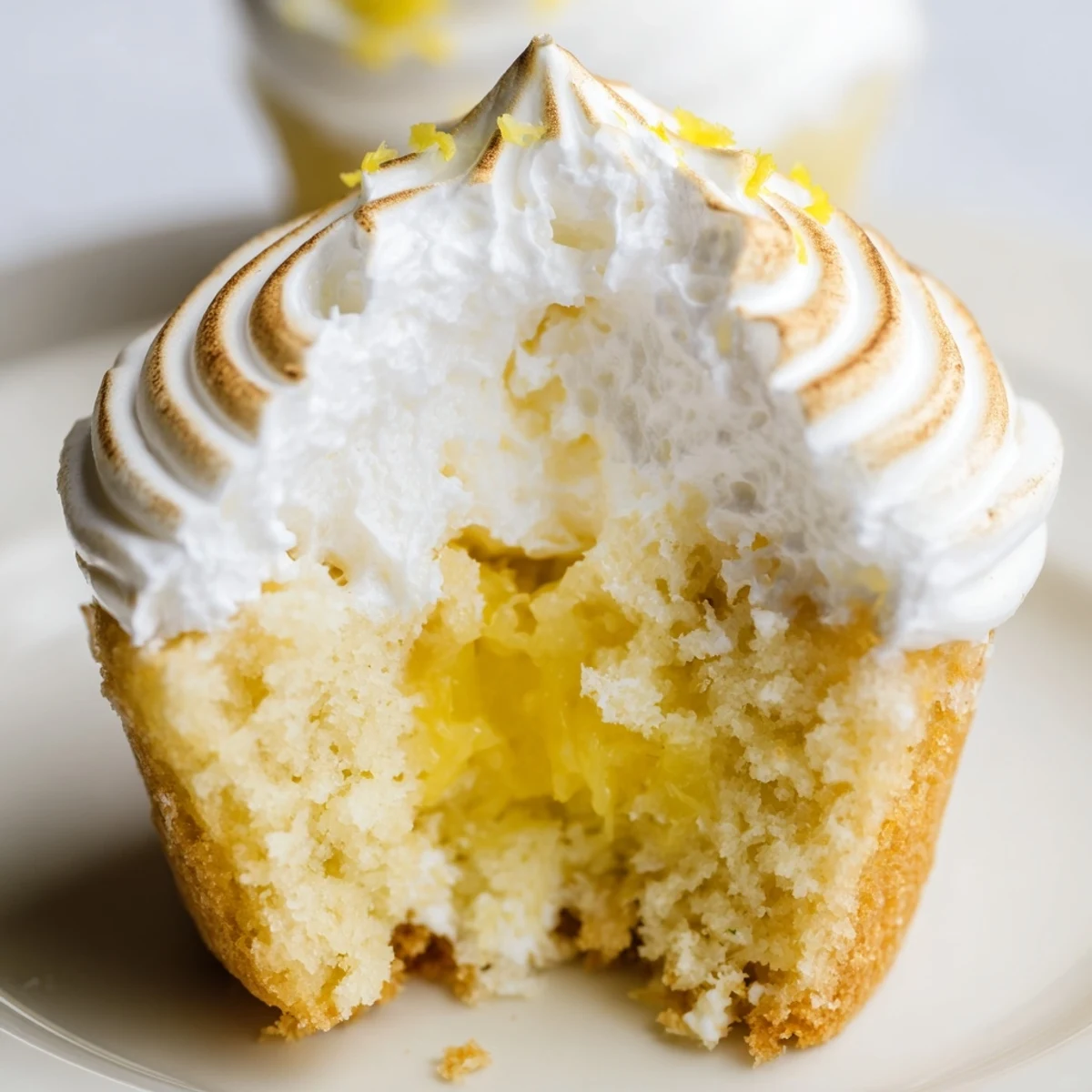 Freshly baked Lemon Meringue Cupcakes with Curd Filling are arranged on a white plate with a vintage lemon squeezer nearby.