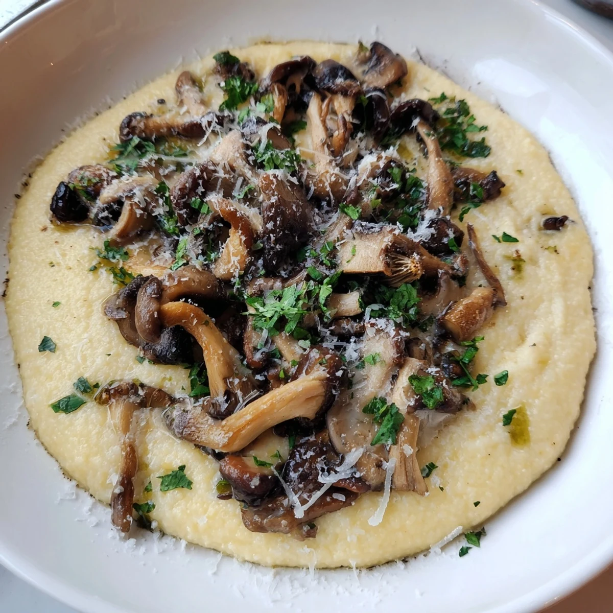 Creamy polenta topped with roasted wild mushrooms, fresh parsley, and parmesan in a rustic white bowl.
