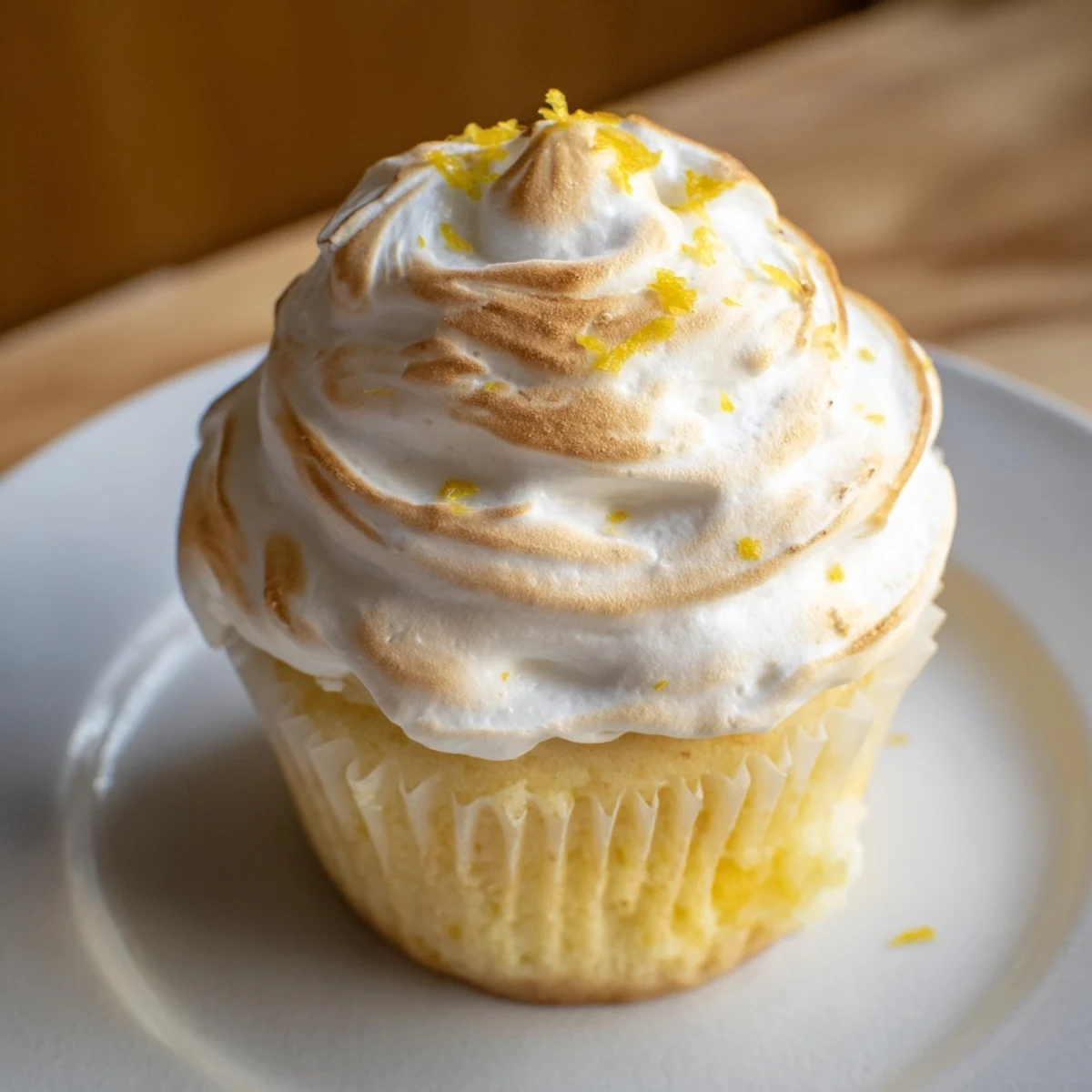 Freshly baked Lemon Meringue Cupcakes sit on a wire rack, showing their golden-yellow crumbs and a bright lemon curd filling peeking from the center.