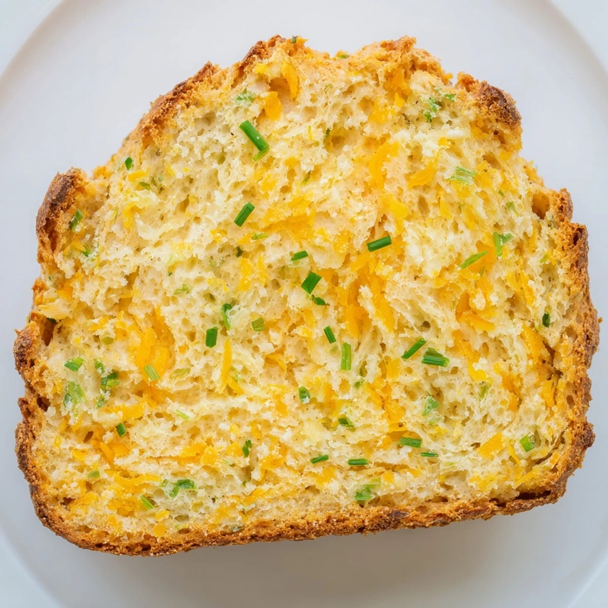 A close-up of warm Savory Cheddar & Chive Irish Soda Bread showing a golden, cheesy crust and tender crumb inside.