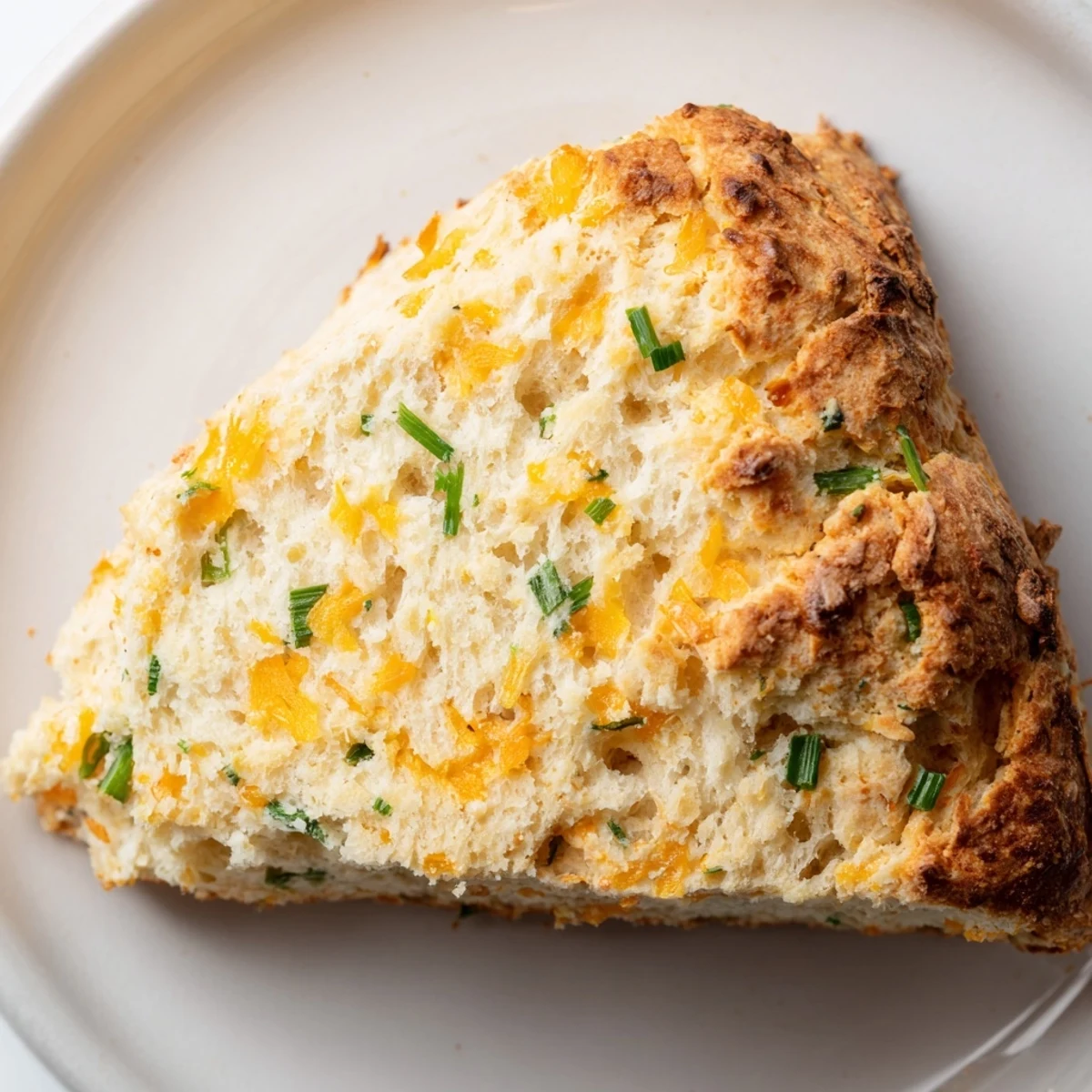 Freshly baked Savory Cheddar & Chive Irish Soda Bread loaf with melted cheddar bits and green chives on a rustic board.