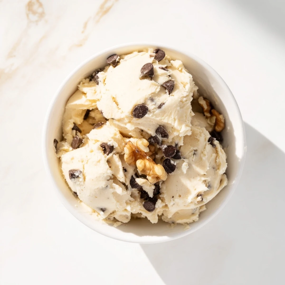 A close-up of Guilt Free Greek Yogurt Cookie Dough in a white bowl, featuring mini dark chocolate chips and chopped walnuts.