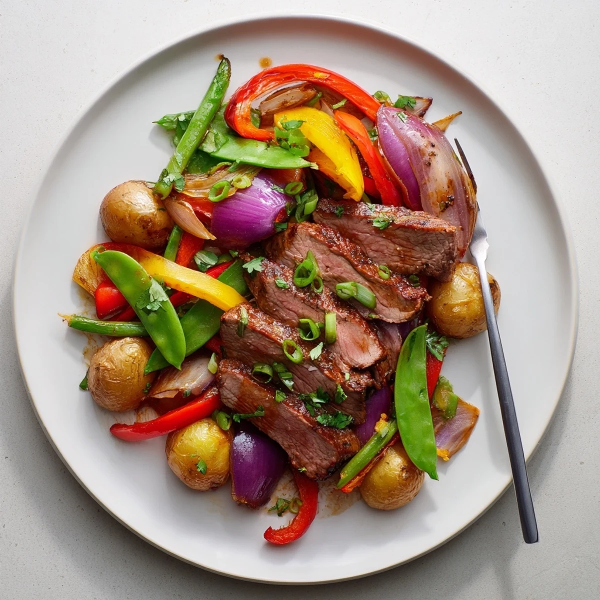 A hearty platter of Blackstone Cowboy Stir Fry Dinner featuring juicy steak, colorful peppers, and golden potatoes, garnished with fresh cilantro and scallions.