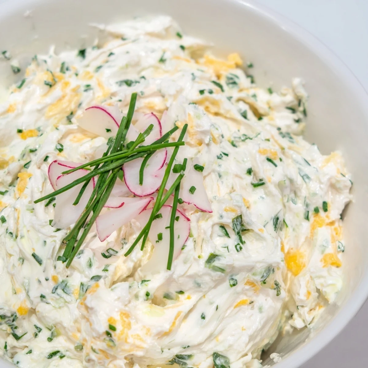 Creamy Simple Easter Herb Cheese Dip with shredded cheddar, topped with radish slices and edible flowers, ready for Easter celebrations on a serving platter.