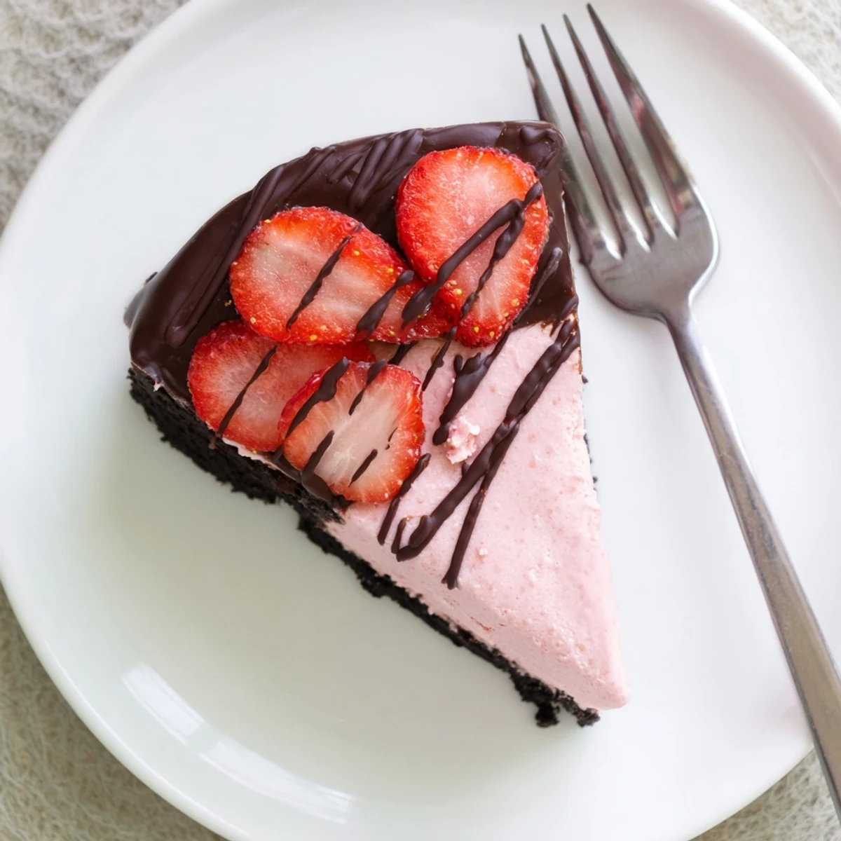 The chilled cheesecake reveals a vibrant pink strawberry filling inside a dark chocolate cookie crust in this slice.