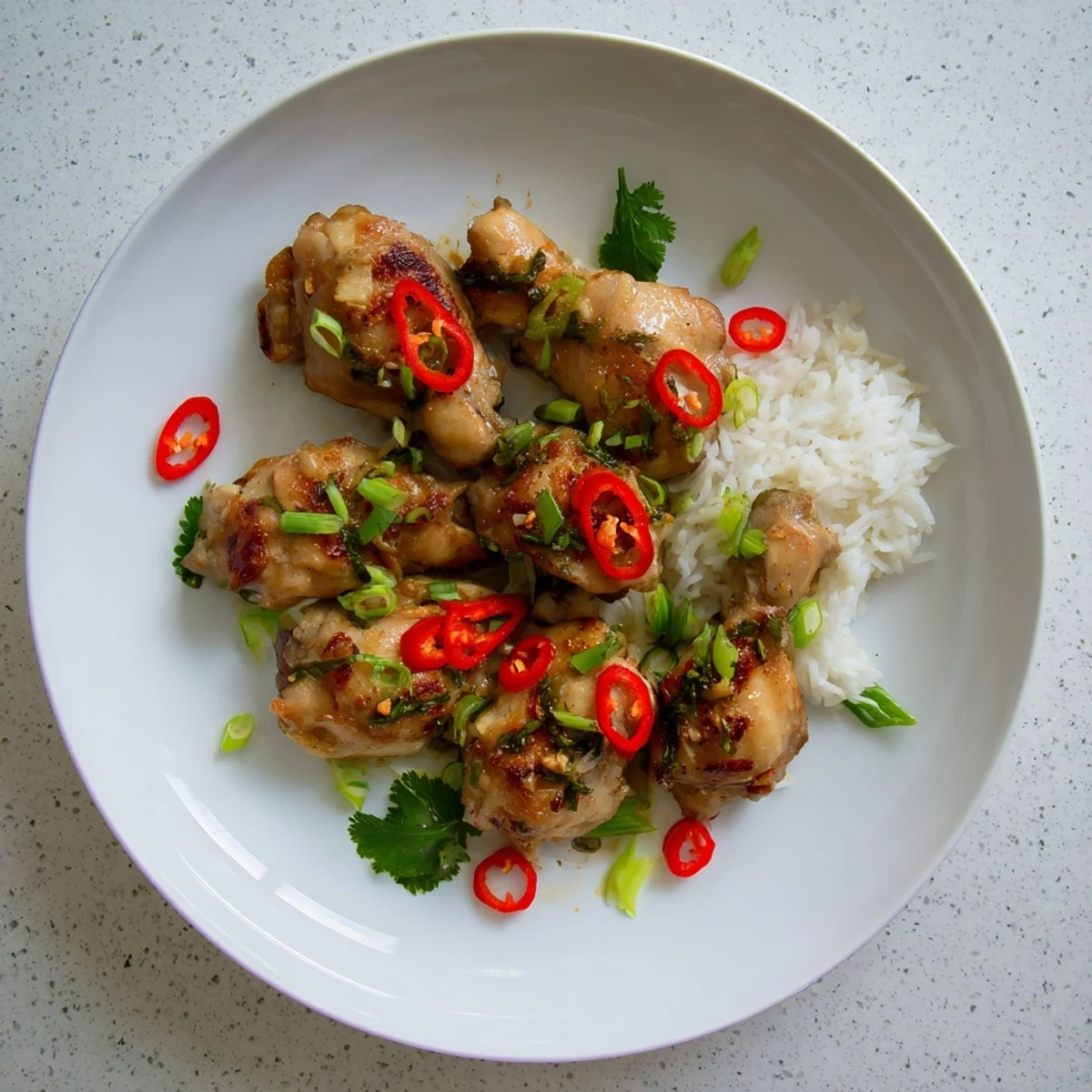 A close-up of tender Vietnamese Lemongrass Chicken garnished with cilantro and red chili slices beside steamed rice.