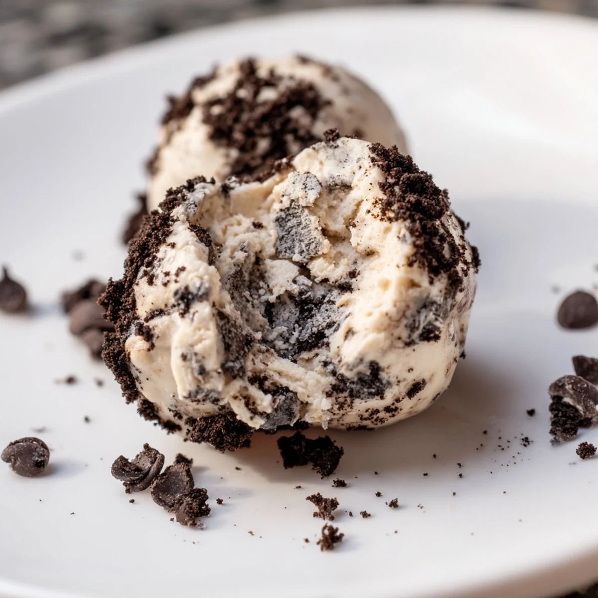 Cream cheese Oreo protein balls rolled in cookie crumbs and garnished with chocolate chips for a no-bake dessert.