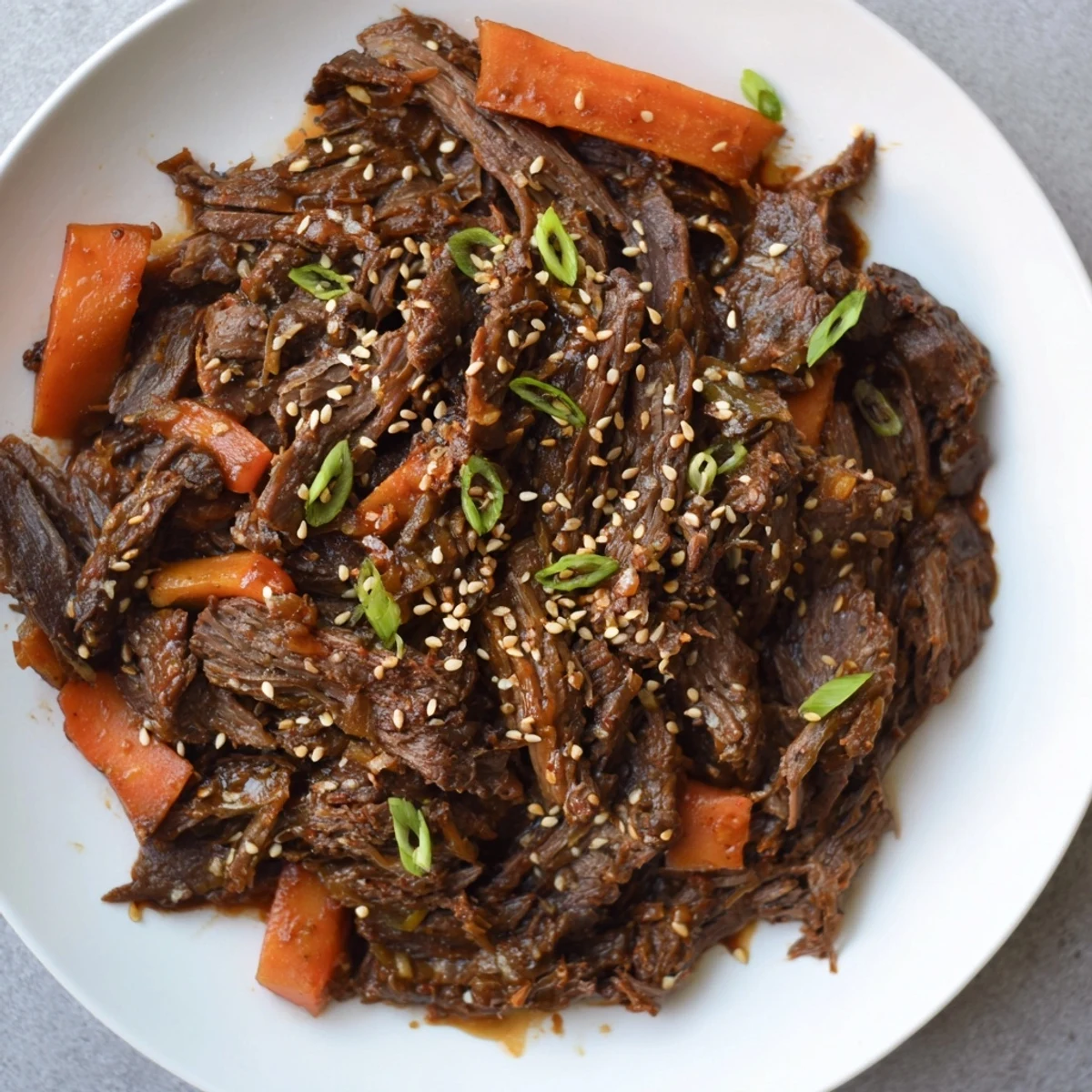 Tender chunks of Korean Style Pot Roast simmered in a glossy, savory-sweet sauce with carrots and daikon on a platter.