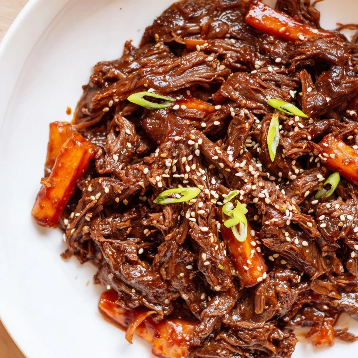 A close-up of shredded Korean Style Pot Roast garnished with sesame seeds and scallions, served alongside steamed rice.