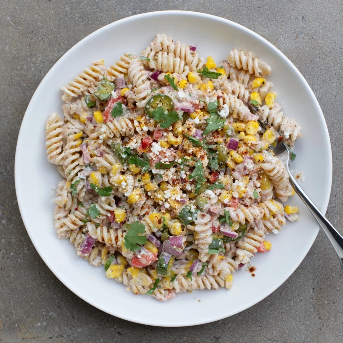Vibrant bowl of Mexican street corn pasta salad garnished with fresh herbs and smoky chili powder