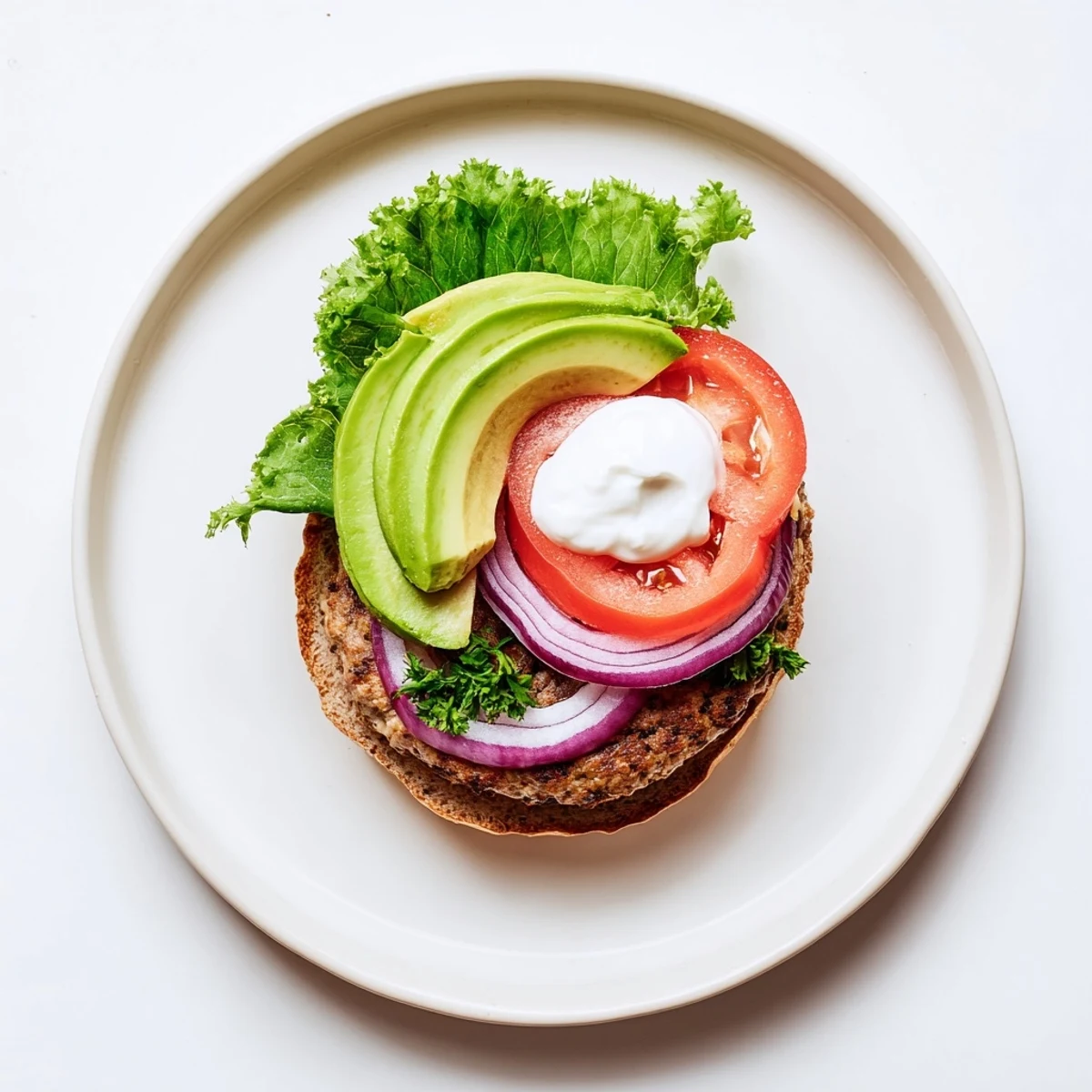 Golden brown healthy high protein burger patty topped with fresh avocado and red onion on a sesame seed bun