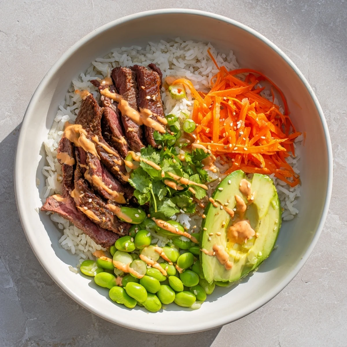 Colorful flank steak bowl featuring tender sliced beef over rice with fresh vegetables and spicy sriracha mayo drizzle