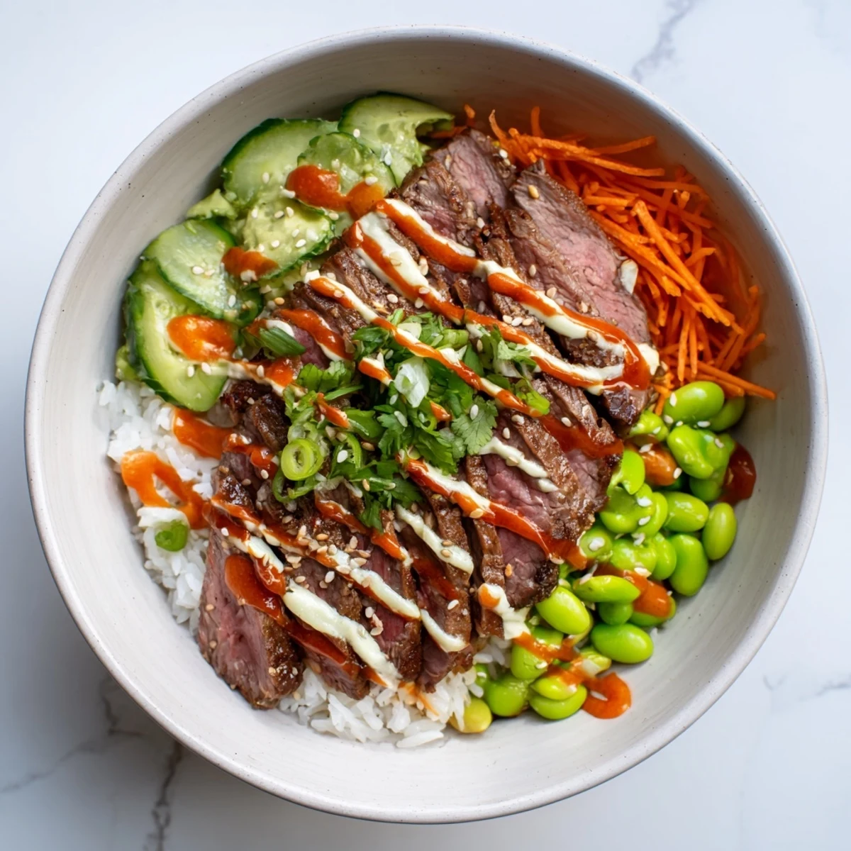 Sizzling flank steak bowl arranged with vibrant carrots, cucumber, creamy avocado slices, and zesty sesame garnish on rice