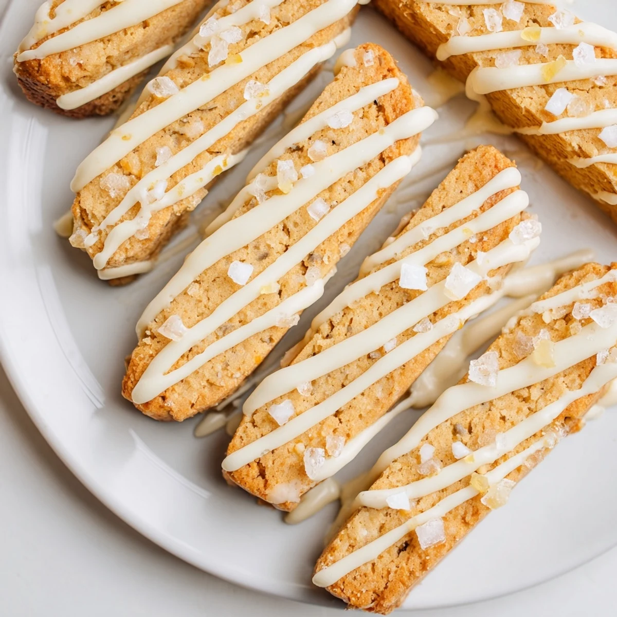 Golden sugar cookie biscotti drizzled with white chocolate on a wooden cutting board