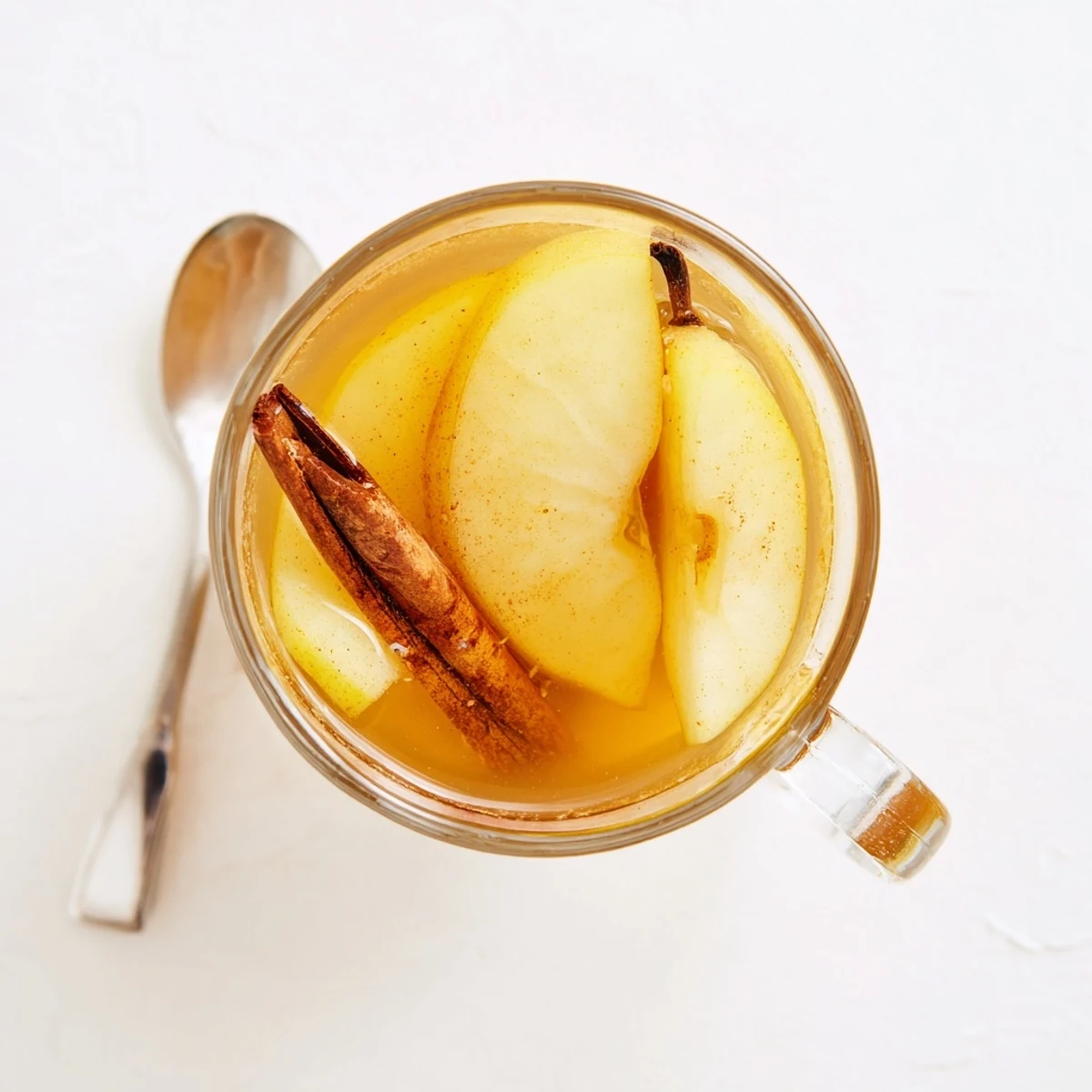 Warm cinnamon pear cider served in clear glass with floating spices and pear garnish