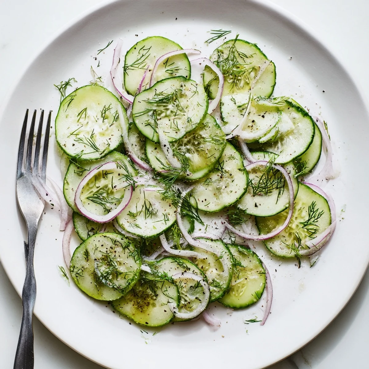 Fresh cucumber salad bowl featuring thinly sliced cucumbers, red onion, and dill in tangy vinegar dressing