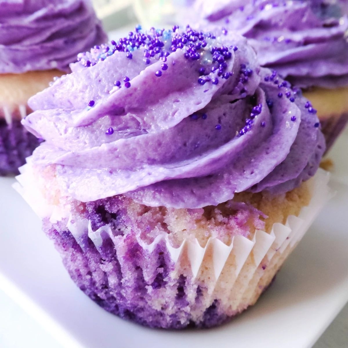 Baked grape soda cupcakes with fluffy grape buttercream swirled high on paper liners, sprinkled with decorations.