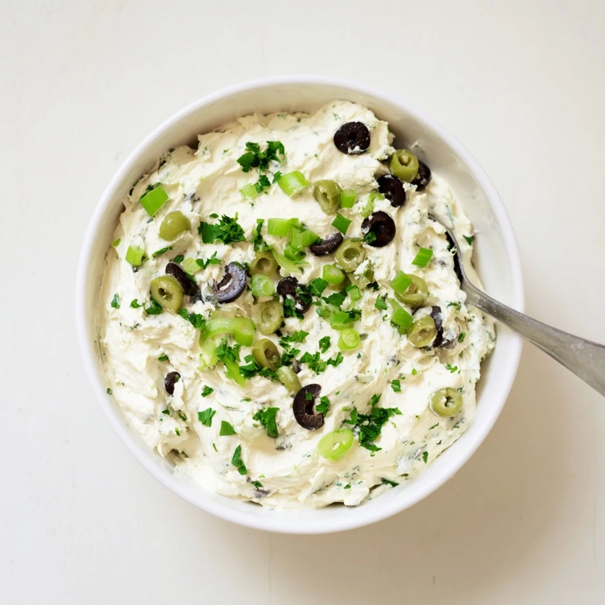 Spoonful of tangy cream cheese olive dip showcasing chopped green and black olives mixed into a smooth, spreadable appetizer.