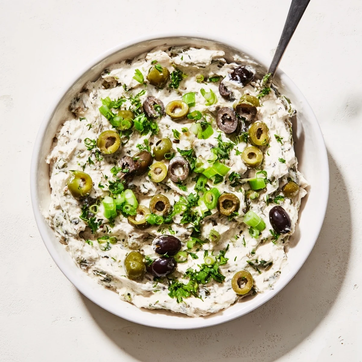 Creamy white olive dip garnished with fresh parsley and green onions, surrounded by crispy crackers for easy party entertaining.