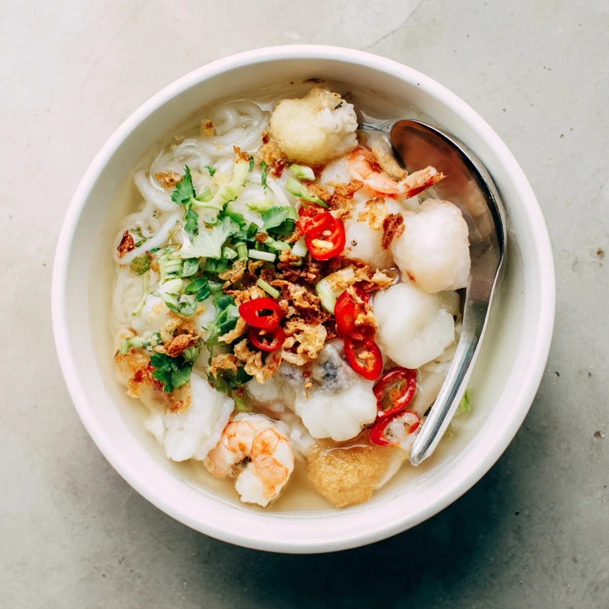 Comforting Vietnamese Banh Canh Cua crab noodle soup served with spring onions, lime wedges, and a sprinkle of black pepper