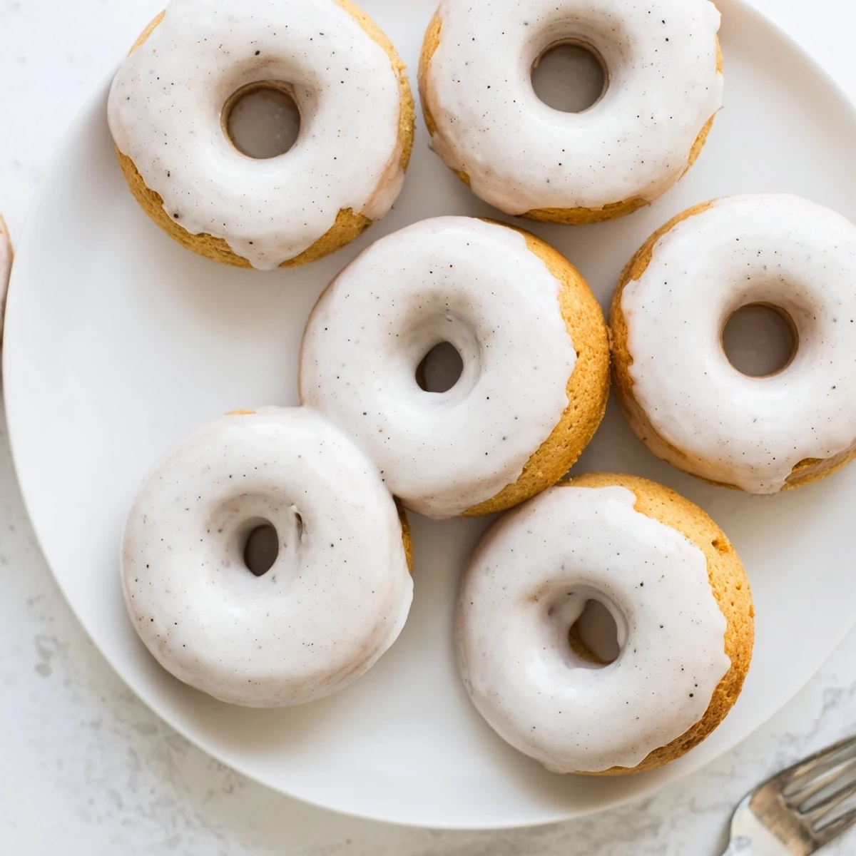 Golden baked Greek yogurt cake donuts topped with sweet vanilla glaze and colorful sprinkles on a white plate