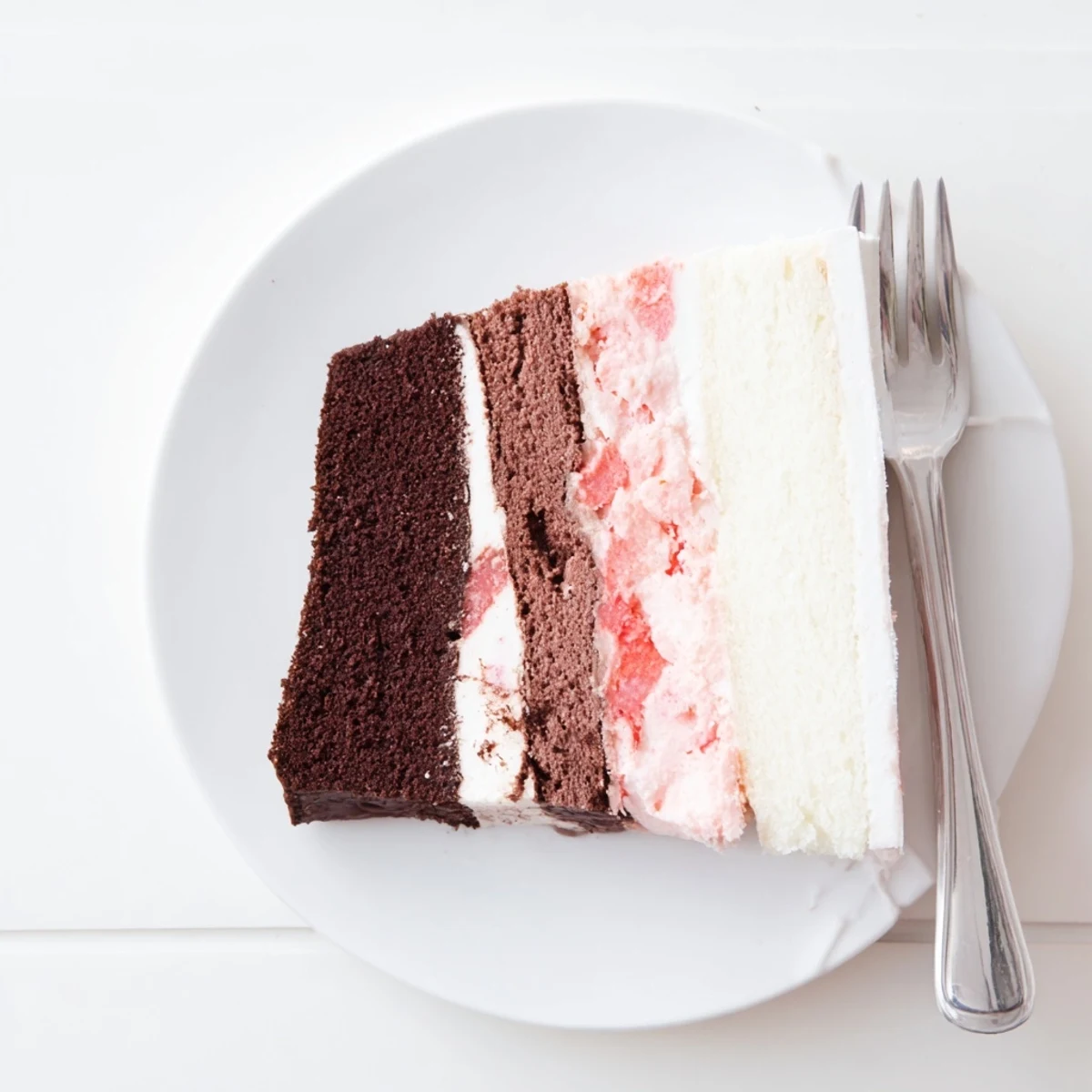 Slice of colorful Neapolitan cake showing chocolate, vanilla, and strawberry layers with creamy buttercream frosting