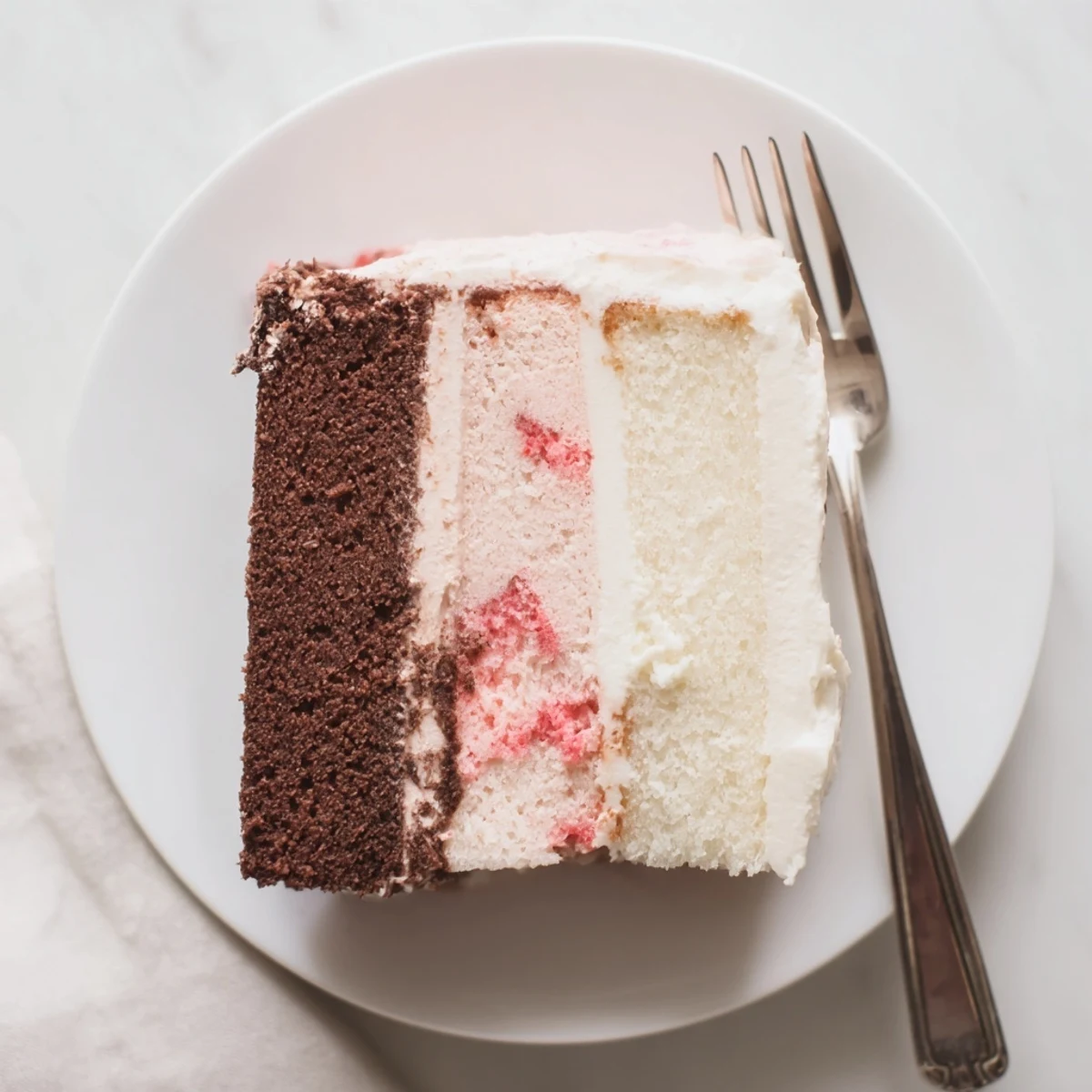 Homemade Neapolitan cake displaying iconic pink, white, and brown horizontal slices on a serving plate