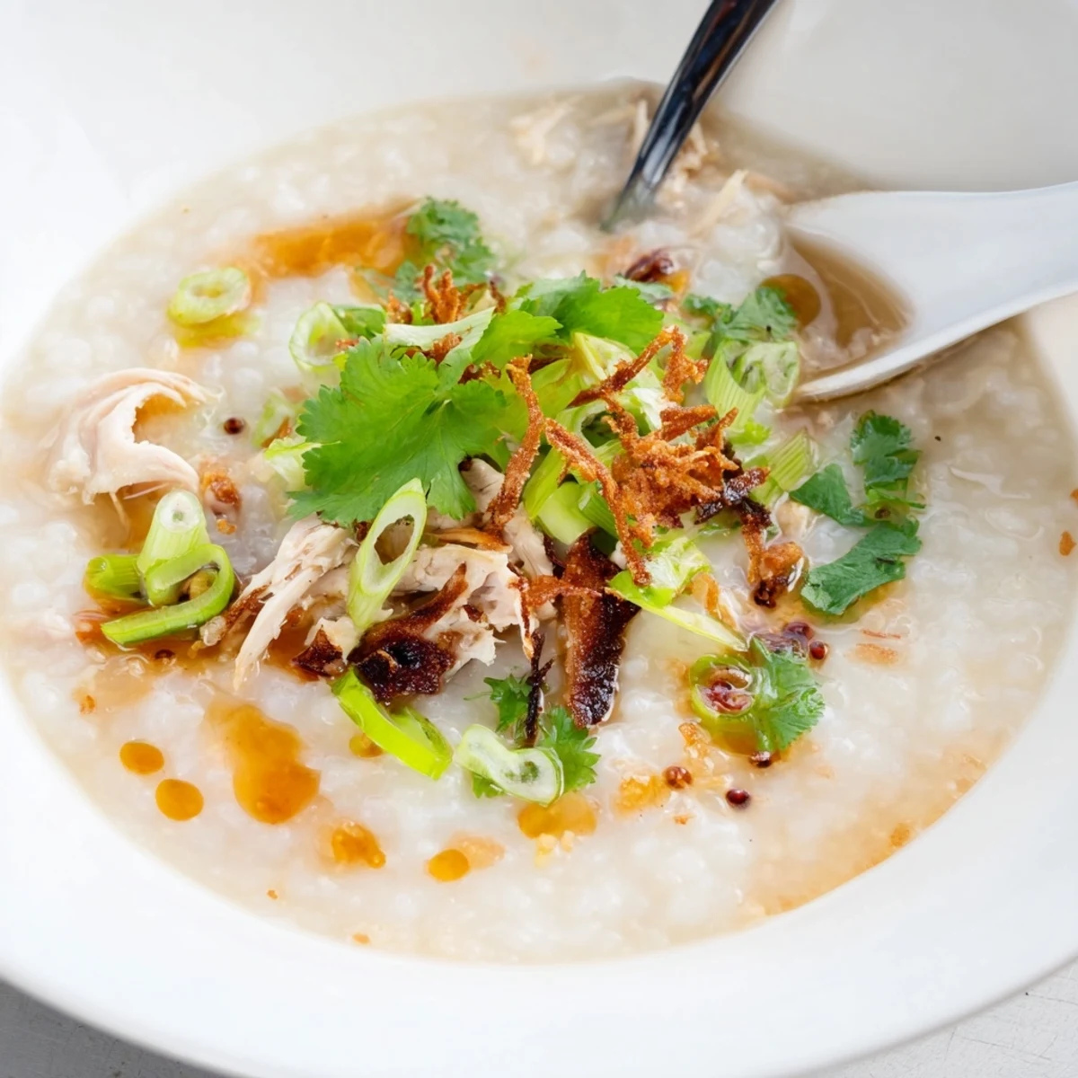 Creamy chicken congee topped with fresh scallions and drizzled with savory sesame oil in a white bowl