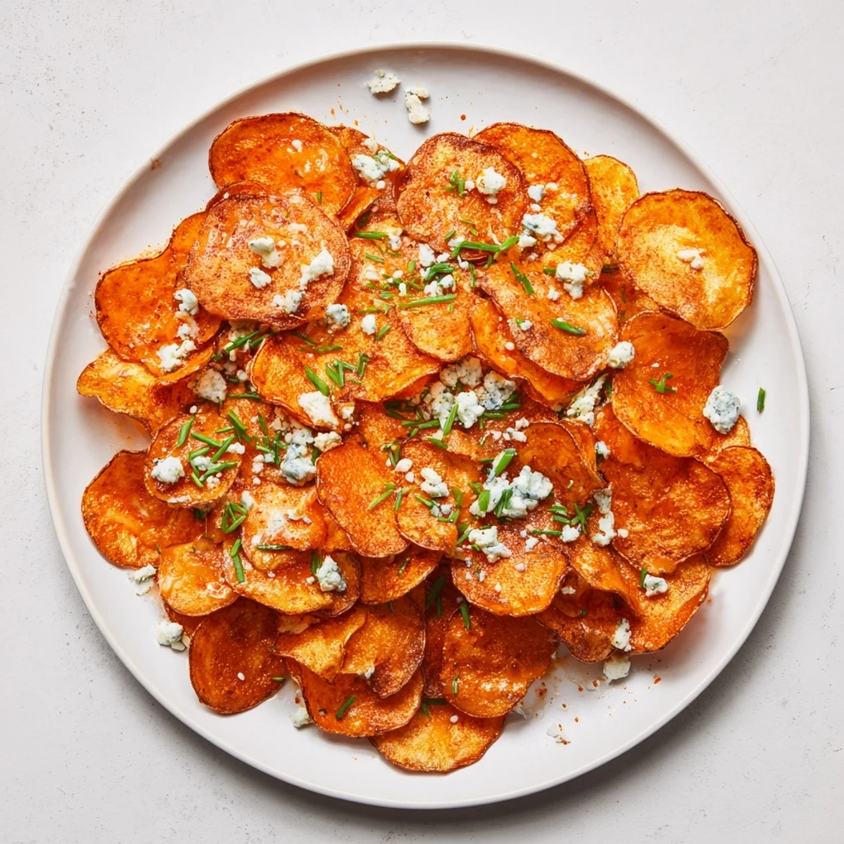 Heap of golden fried potato chips coated in tangy Buffalo sauce with blue cheese crumbles on top