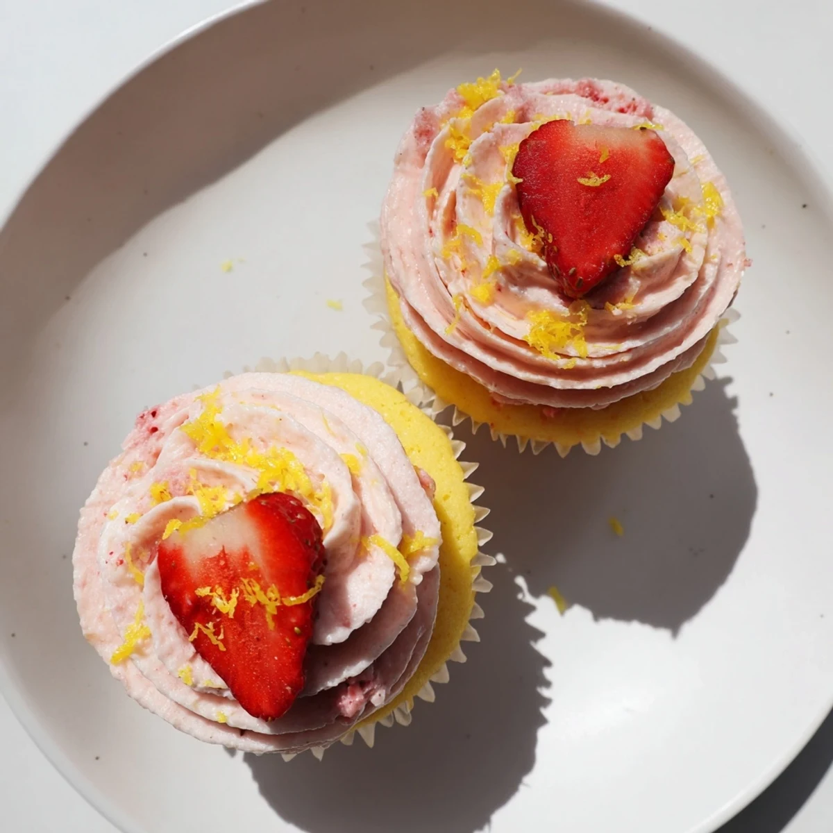Fresh strawberry lemonade cupcakes topped with pink strawberry frosting and garnished with lemon zest