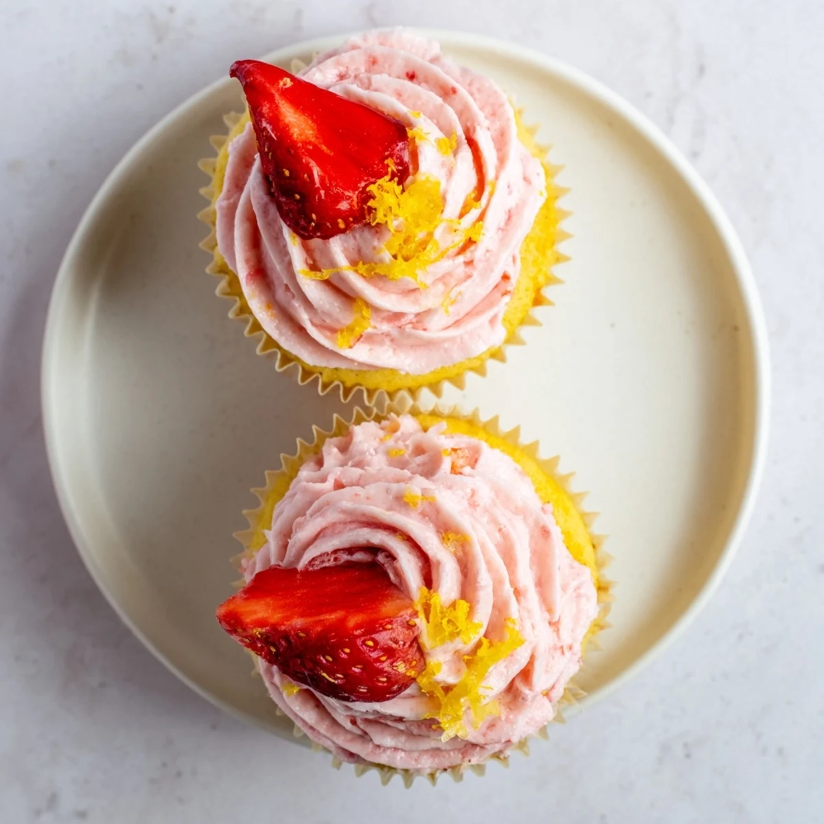Golden strawberry lemonade cupcakes with vibrant pink strawberry buttercream and fruity garnish on plate