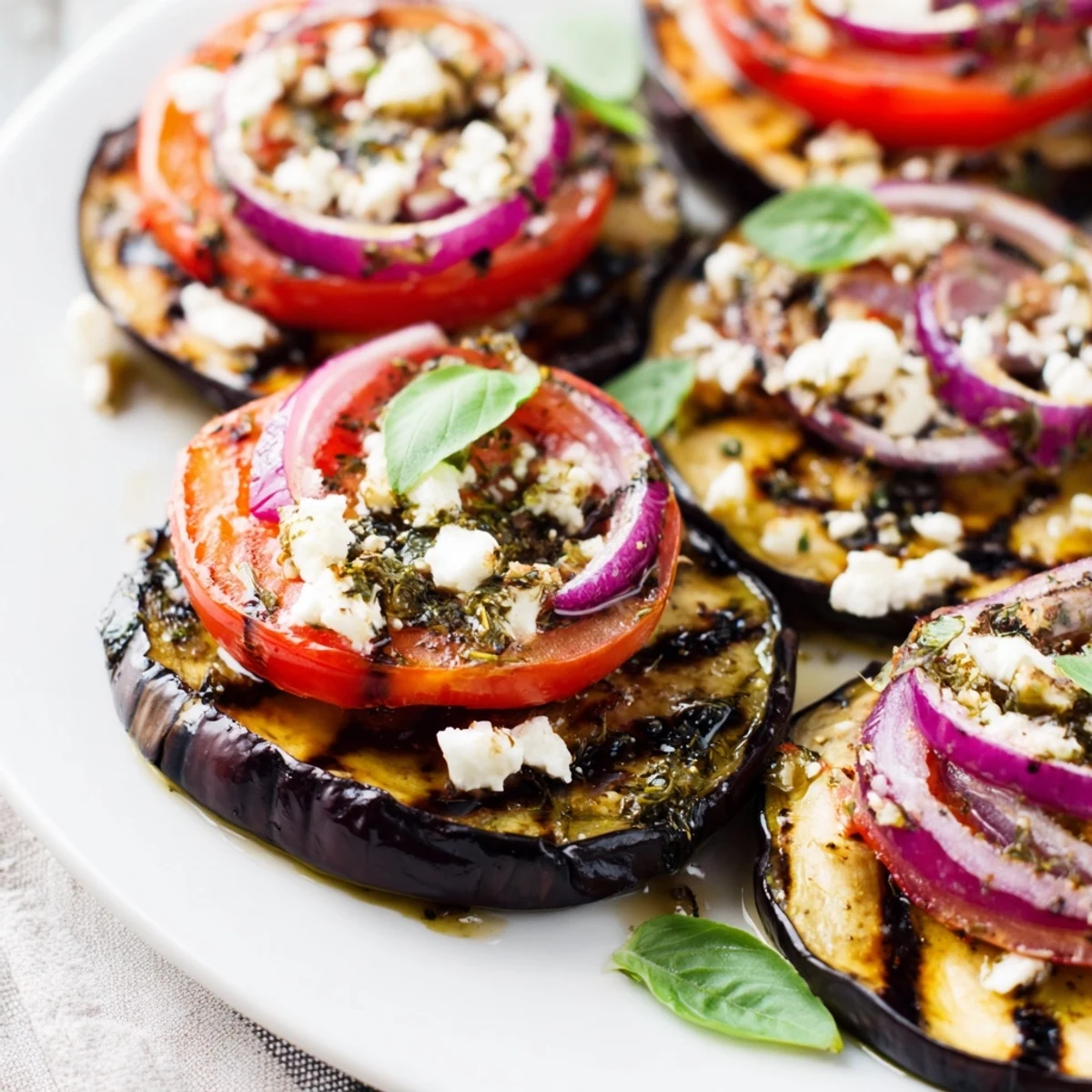 Smoky grilled tomato eggplant layered on a platter with fresh basil and crumbled feta