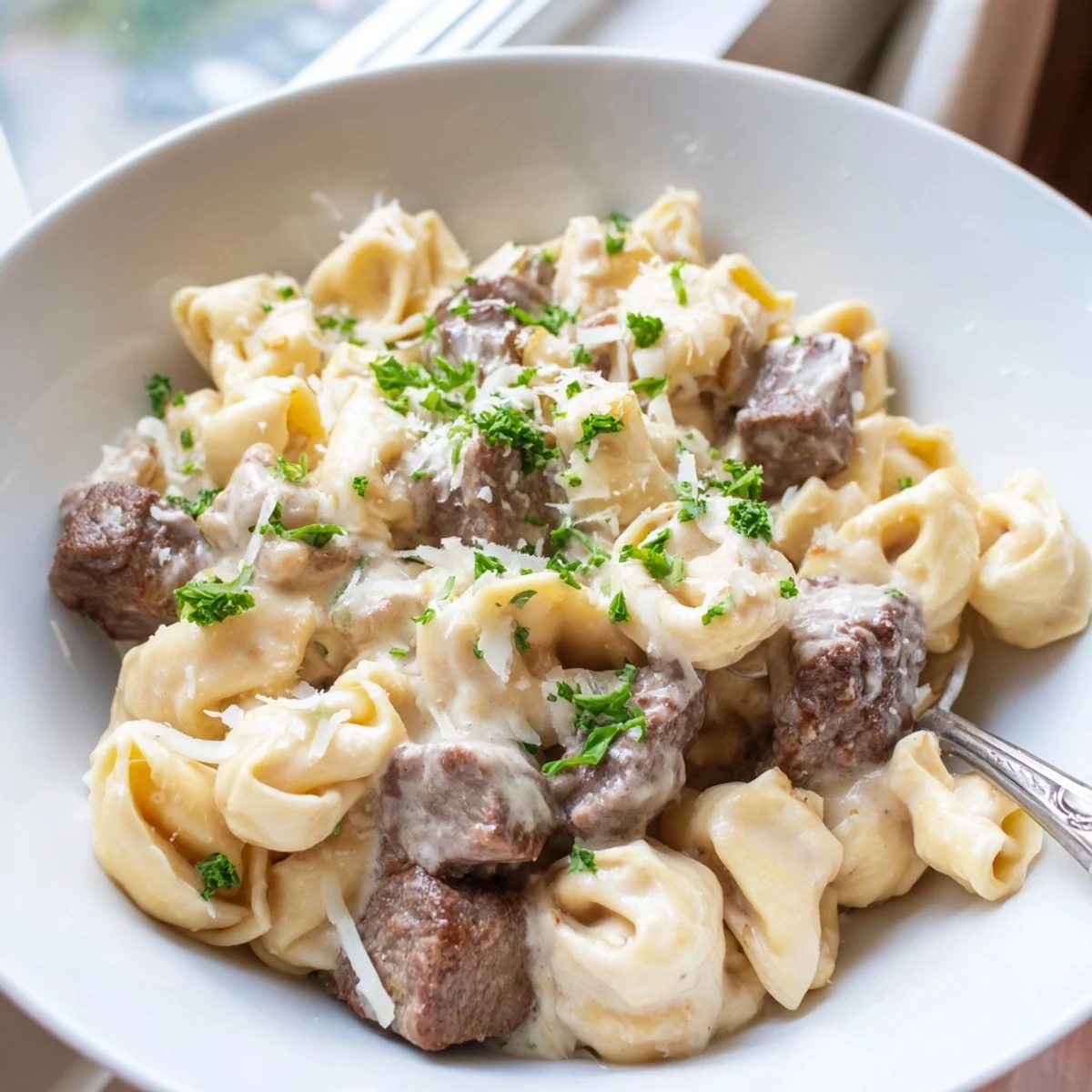 Garlic steak tortellini plated in a creamy white bowl with fresh parsley